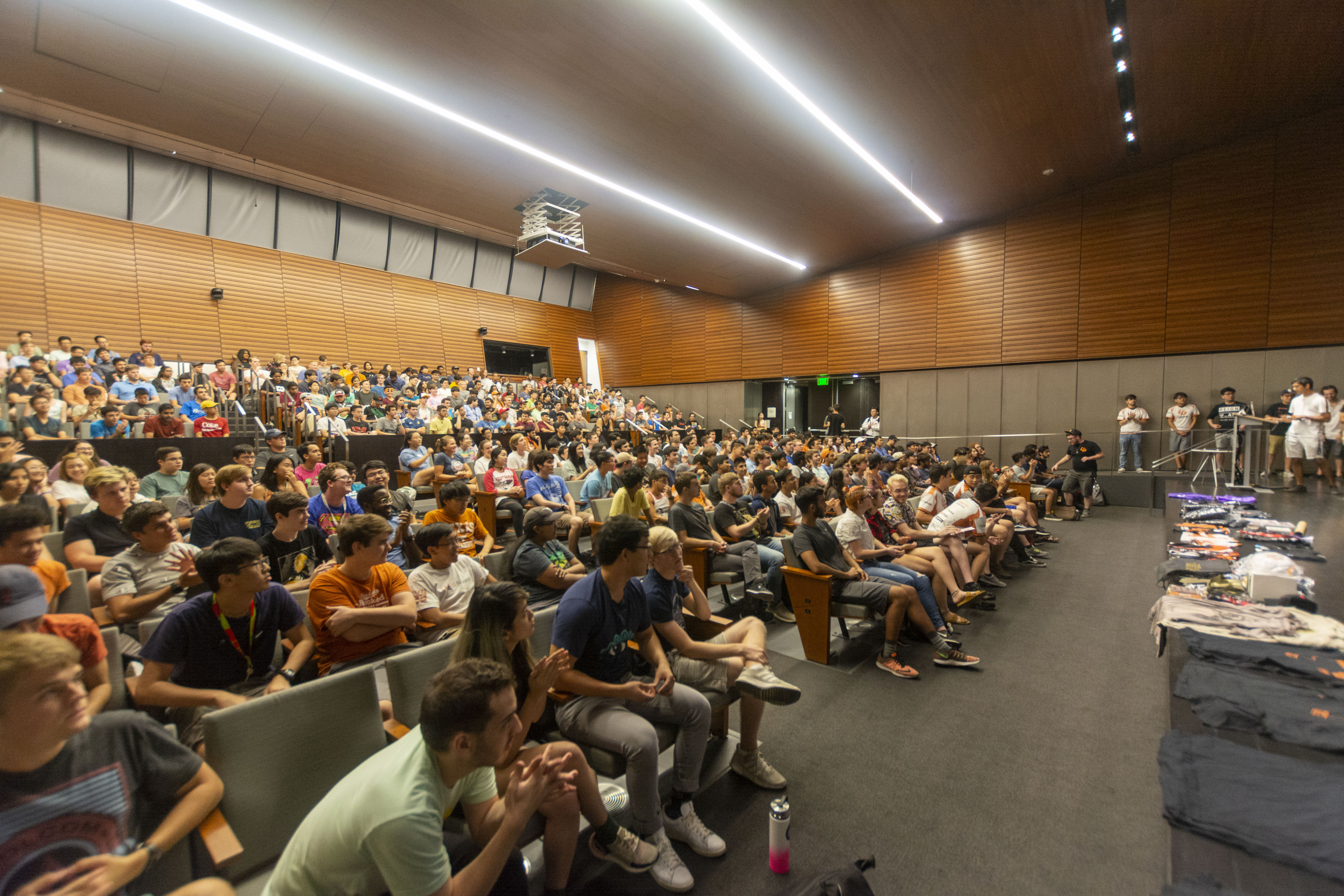 An auditorium full of college students. Every seat in the room is occupied. Some people stand to the side and on the stairs.